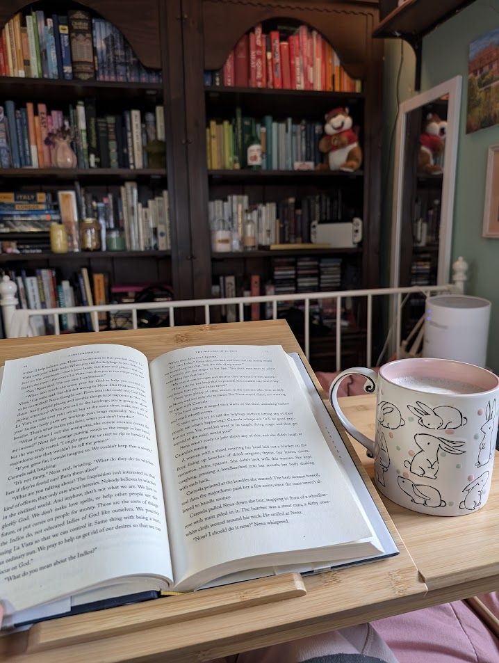 My open book and my cup of tea with my filled bookshelves in the background