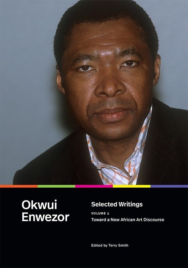 Cover of Toward a Selected Writings, Volume 1: New African Art Discourse by Okwui Enwezor, edited by Terry Smith. The cover features a close-up photograph of Okwui Enwezor, wearing a dark suit and patterned shirt, with a calm expression. Below the image, the title and editor information are displayed on a black background, complemented by a colorful horizontal stripe running across the top, adding a modern and dynamic element.