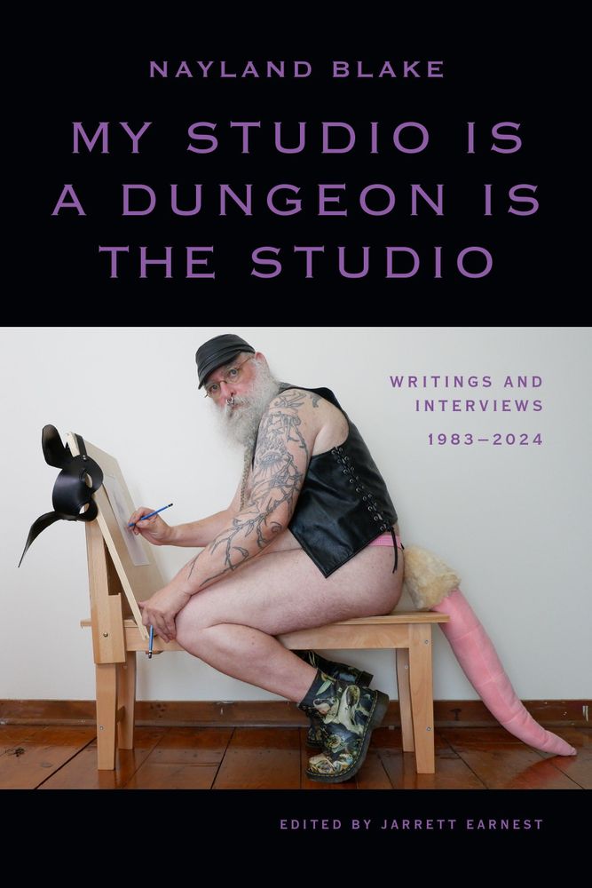 Cover of My Studio is a Dungeon is the Studio by Nayland Blake, edited by Jarrett Earnest. A photograph shows the author wearing a black leather cap and vest, glasses, and pink underwear with a furry tail attachment. They are at an easel with a black rabbit mask hanging on a corner. They have an intricate tattoo sleeve on their left arm. The book title is in large purple text on a black background at the top. 