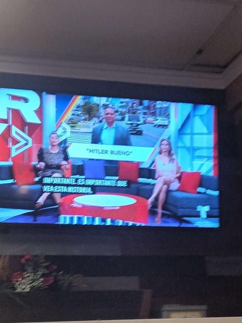 mexican news talk show, two ladies on a couch with a picture of a man in the suit behind them with the title HITLER BUENO underneath
