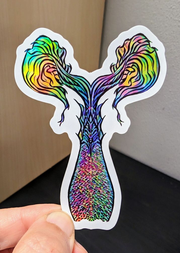 Photo of a left hand holding a diecut sticker. The sticker is a holographic mermaid tail drawing.