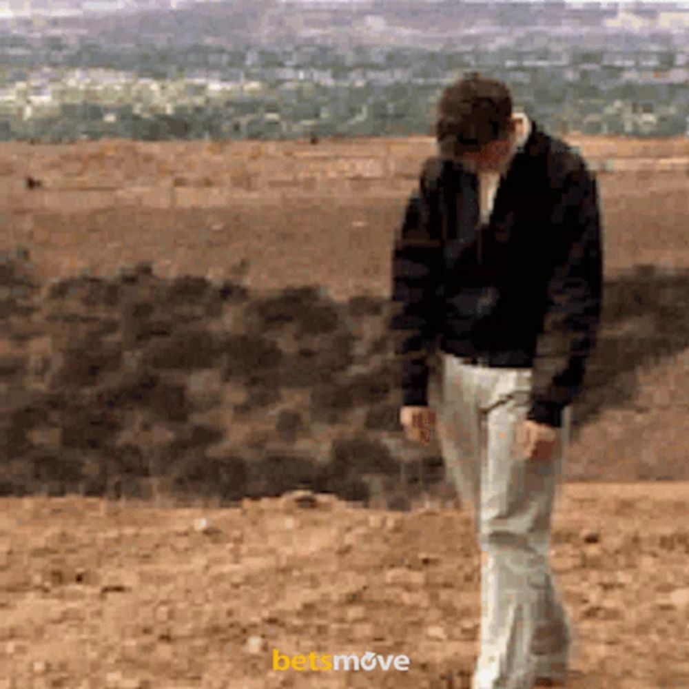 a man in a black jacket and white pants is walking on a dirt field with the word betmove visible in the corner