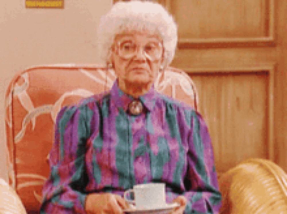 an elderly woman is sitting in a chair holding a cup and saucer