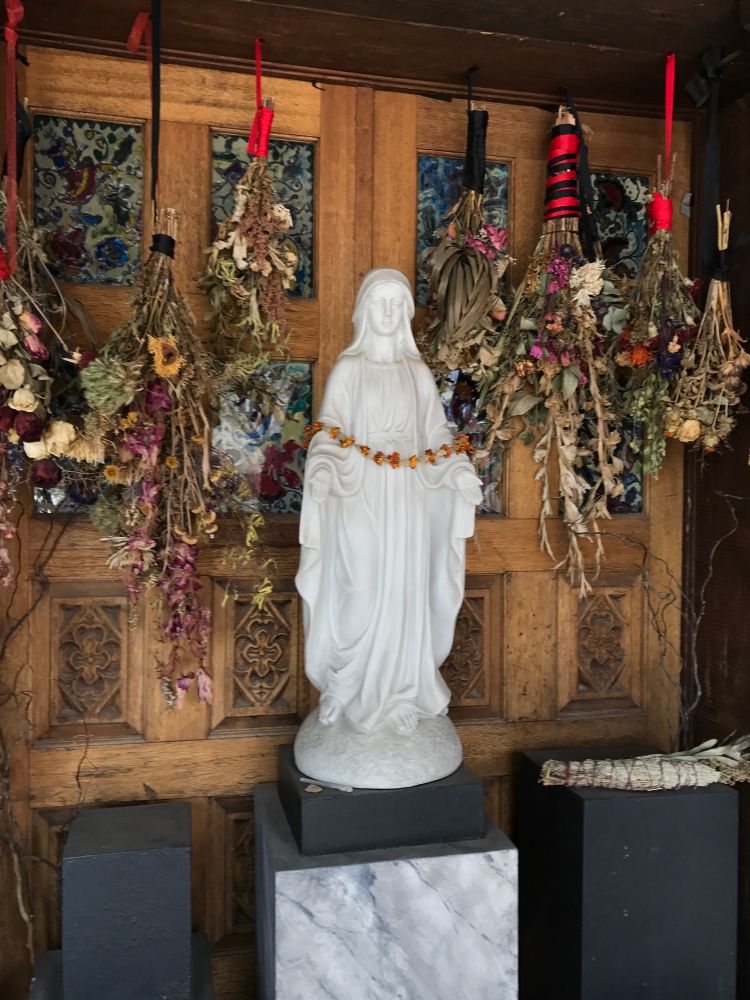 A statue of Virgin Mary surrounded by bushels of dried flowers & sage