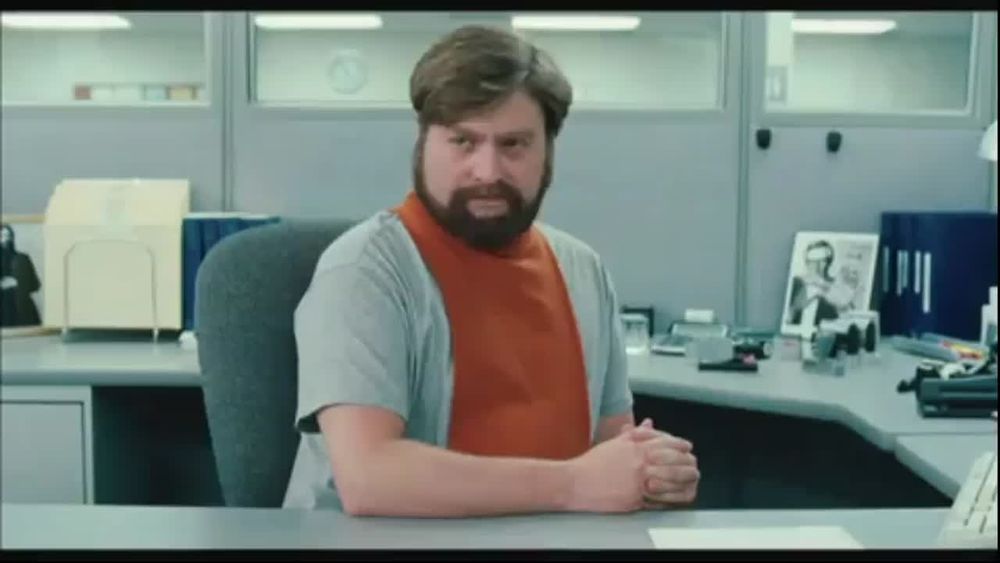 Man with a beard and an orange dickie in an office. 