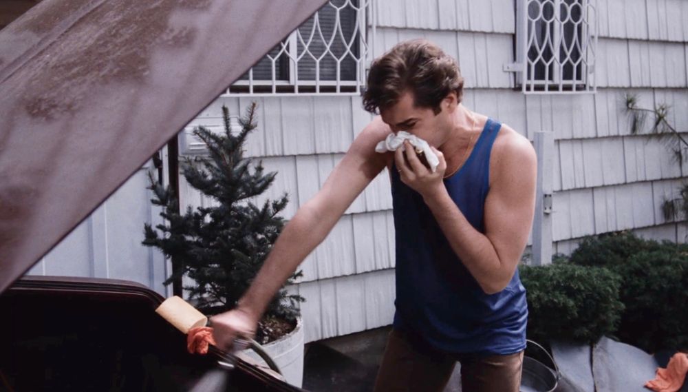 Ray Liotta as Henry Hill from Goodfellas, holding a cloth to his face and using a hose to wash the stink of a rotted corpse from his car.