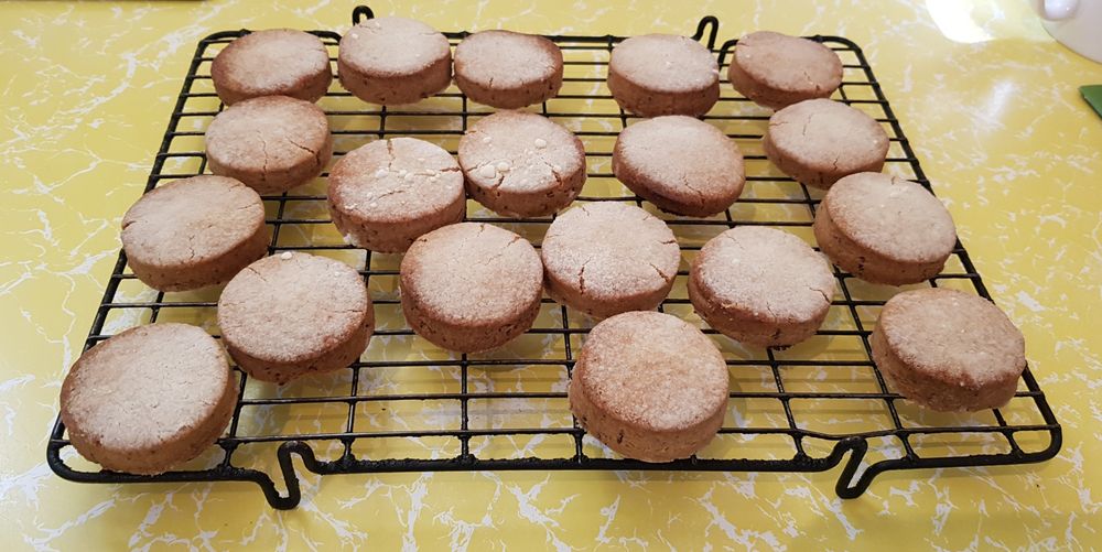 A batch of Goosenargh Cakes cooling on a wire rack on a yellow kitchen counter.