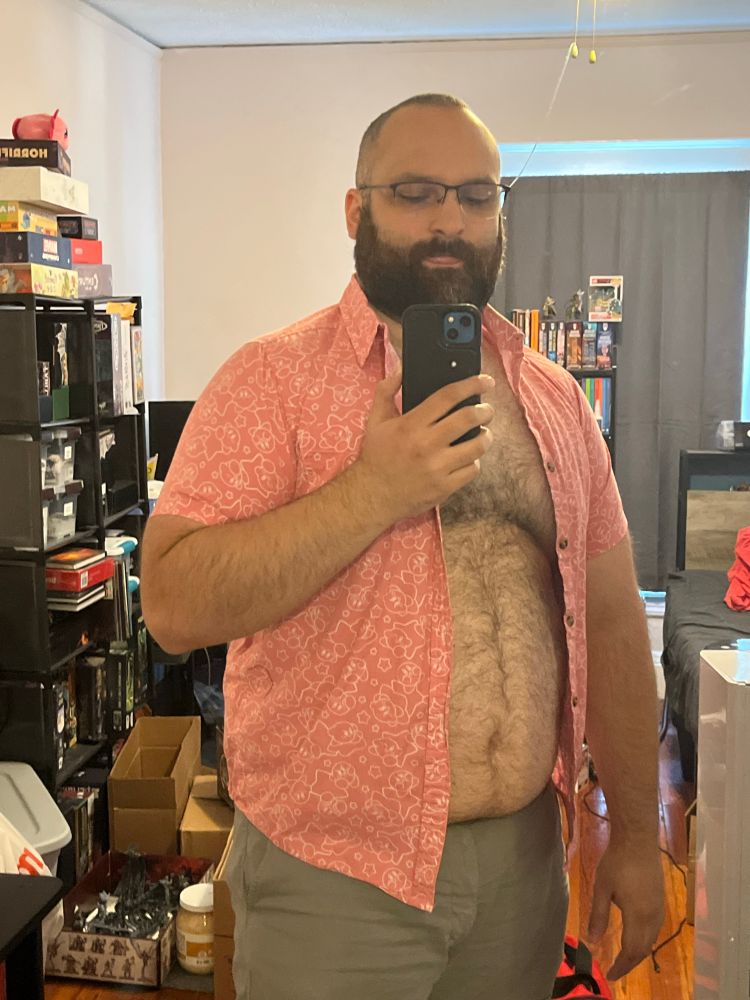 Gay hairy fat man in a pink Kirby shirt and grey shorts questioning his life choices