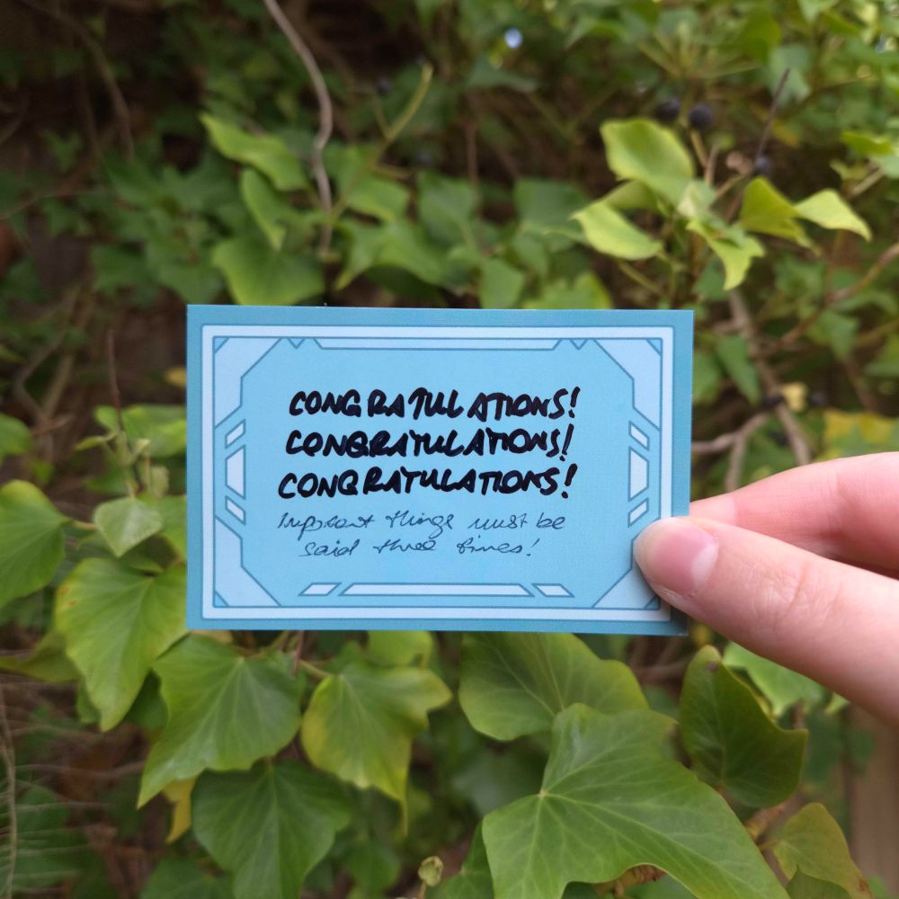 A photo of the writeable system card sticker with a handwritten message. In permanent marker "congratulations!" is written three times in capital letters, and below that in ballpoint pen and in cursive is "important things must be said three times!"