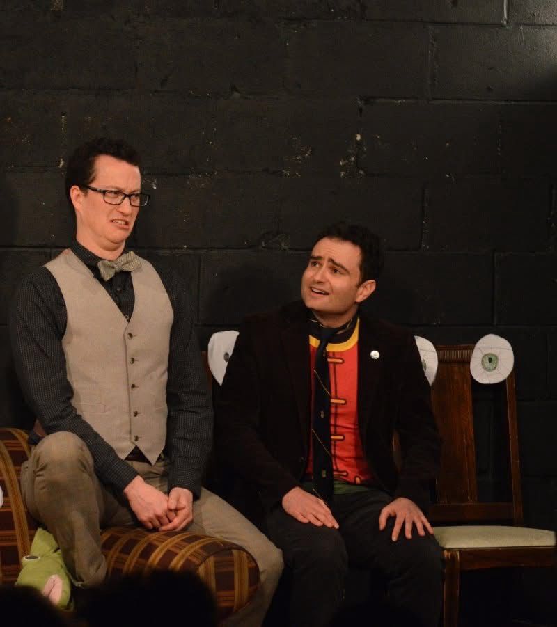 Owen in a bow tie and Louie in his tshirt and tie sit on chairs with eyes