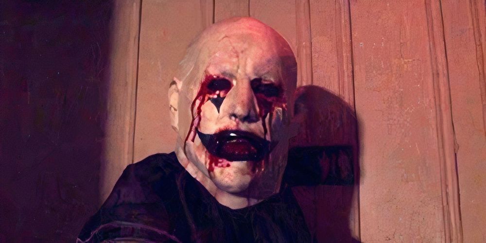 A still from 2015 found footage horror film, "Hell House LLC". A person wearing a gory clown mask with no visible eyes faces the camera, ominously. 