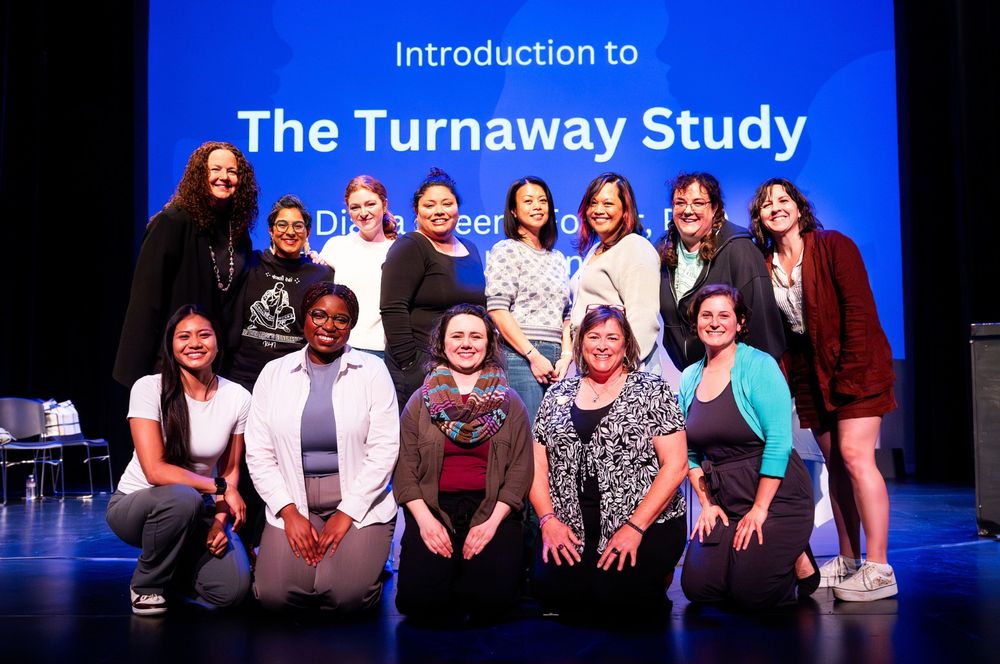 A group of 13 people standing in 2 rows in front of a slide that reads "Introduction to The Turnaway Study"