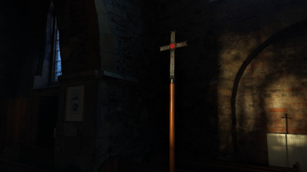 A metal cross on a wooden pole, illuminated by a shaft of sunlight 