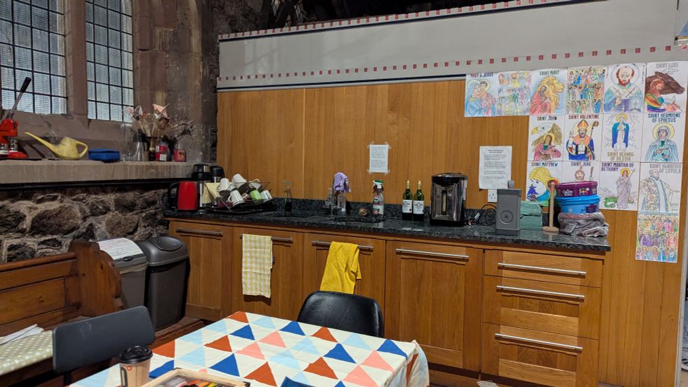 The eastern part of the north aisle of St nicks showing a cluttered windowsill, a countertop with sinks and a kettle, and colouring in stuck to the wooden backsplash 
