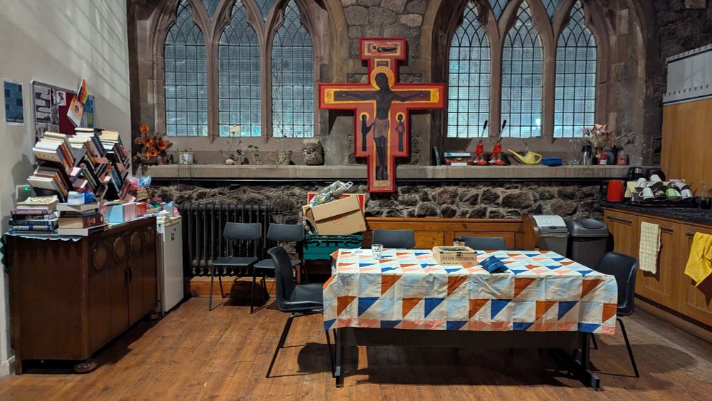 The north aisle of St Nicholas church, with plastic chairs strewn everywhere, a large desk used as a table, piles of books, and a large cross