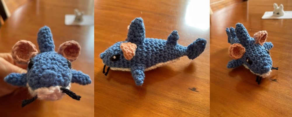 a small crochet plush of a blue shark with pink mouse ears and black whiskers