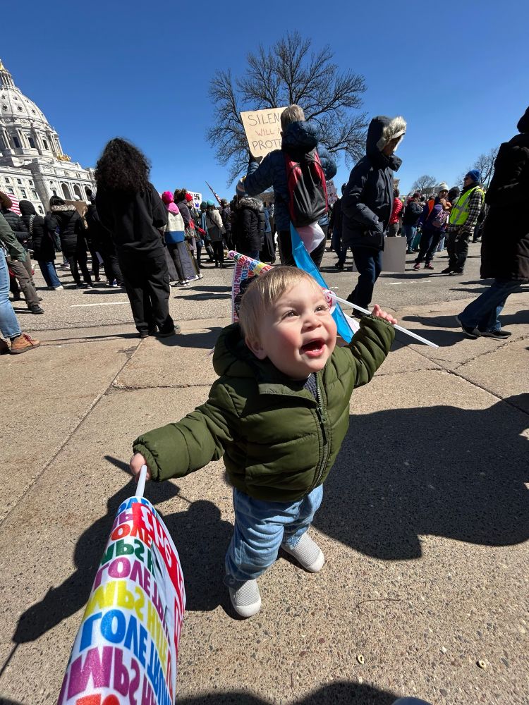 Leo, a toddler, yelling and waving protest flags in a crowd in front of the Capitol