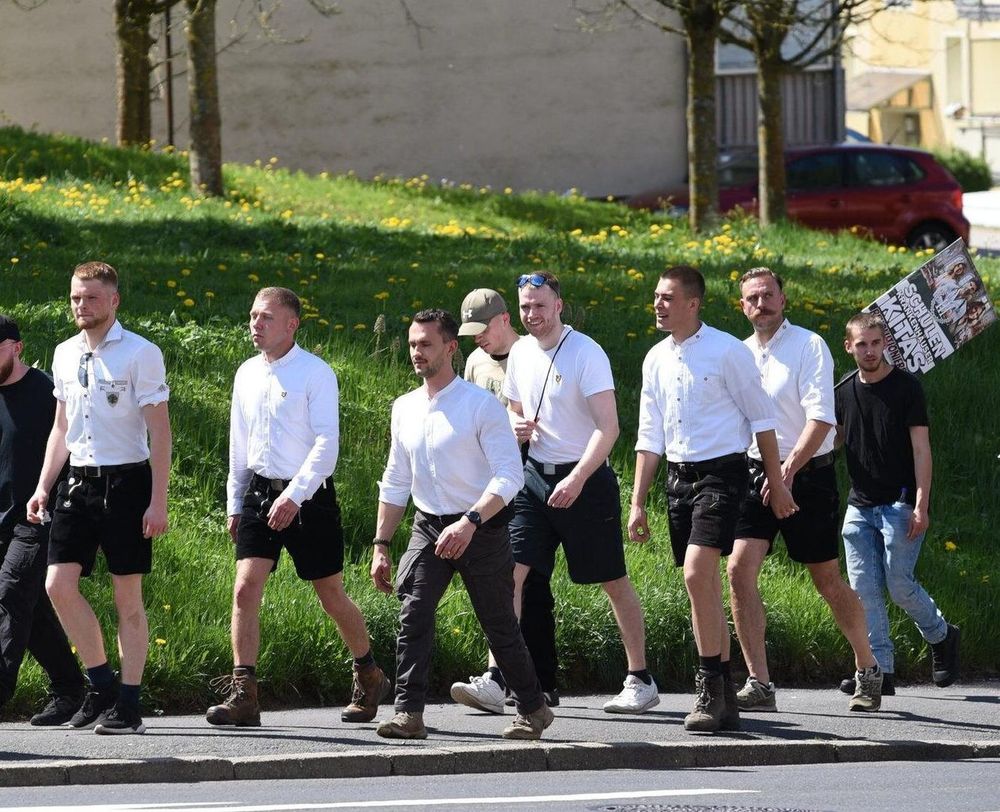 01.05.25, Suhl: Neonaziaufmarsch organsiert von „Der Dritte Weg“. Zu sehen ist eine Gruppe Neonazis in schwarzen Hosen und weißen Hemden, die im hinteren Teil der Neonazi-Demo über einen Gehsteig gehen. Mit dabei, mit fünf Personen, die Aktion Hermannsland in weißen Hemden. V.l.n.r.: Dennis Hopp, unbek., unbek., Justin Steiger, Lennard Sanner (Quelle: Pixelarchiv)