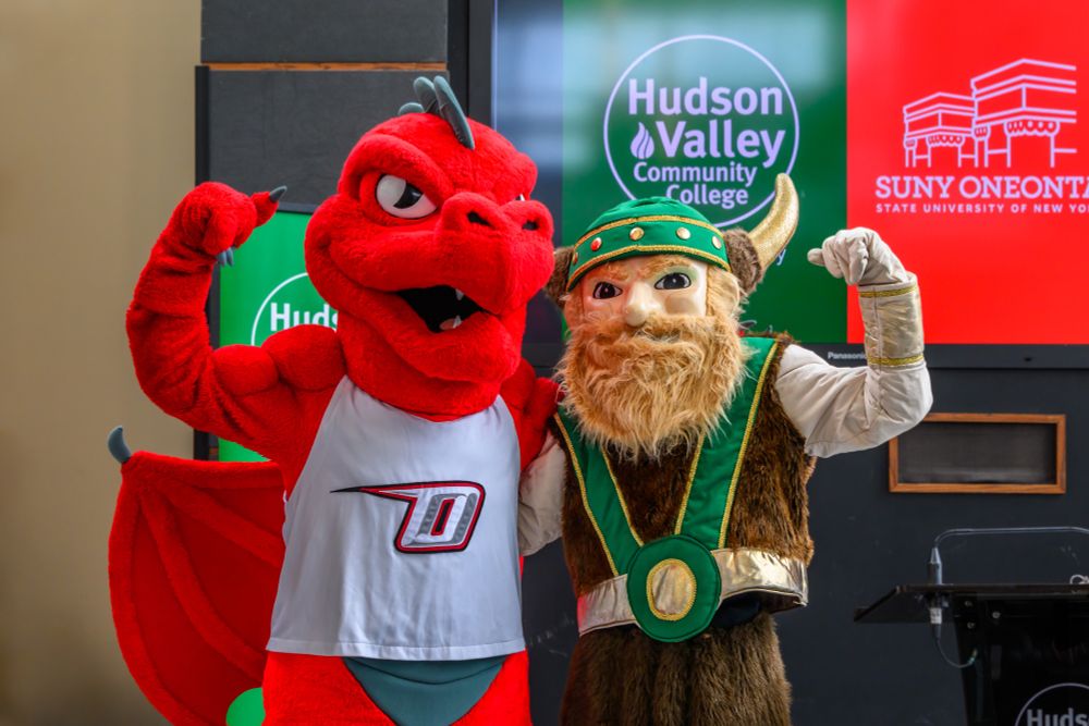 The mascots of Hudson Valley Community College and SUNY Oneonta pose together in front of school signage