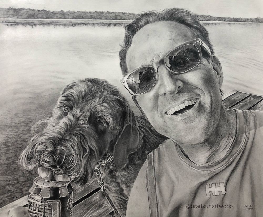“Cooper and Paul” is an 11x14” graphite drawing of a man and his beloved labradoodle standing on a boat dock in front of a lake. The dog is licking the top of Paul’s beer can. Paul is smiling.