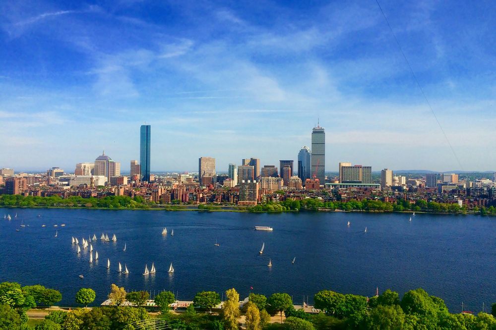 View of the Boston city skyline across a river. It’s a bright day and there are sailboats on the river