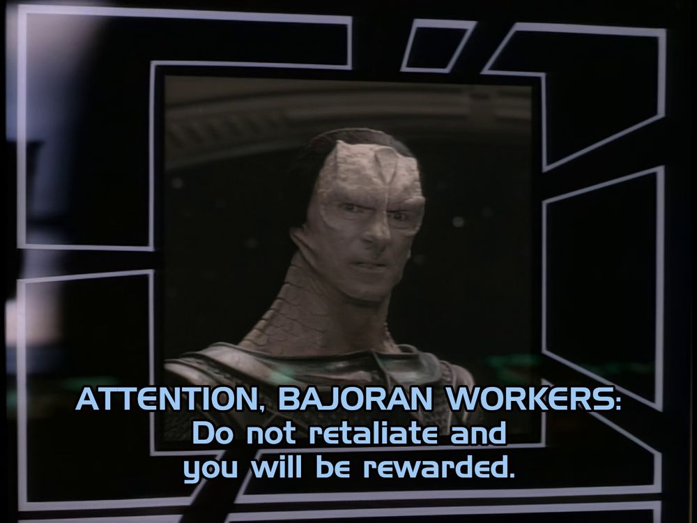 An image of Seagul Dukat, an alien with grey scaley skin, on a screen. A caption reads "ATTENTION BAJORAN WORKERS: Do not retaliate and you will be rewarded."