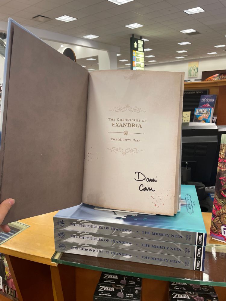 A large book sits atop three other copies on a desk at Barnes & Noble. The pages are a light cream color, and beneath the title text is Dani Carr’s signature!