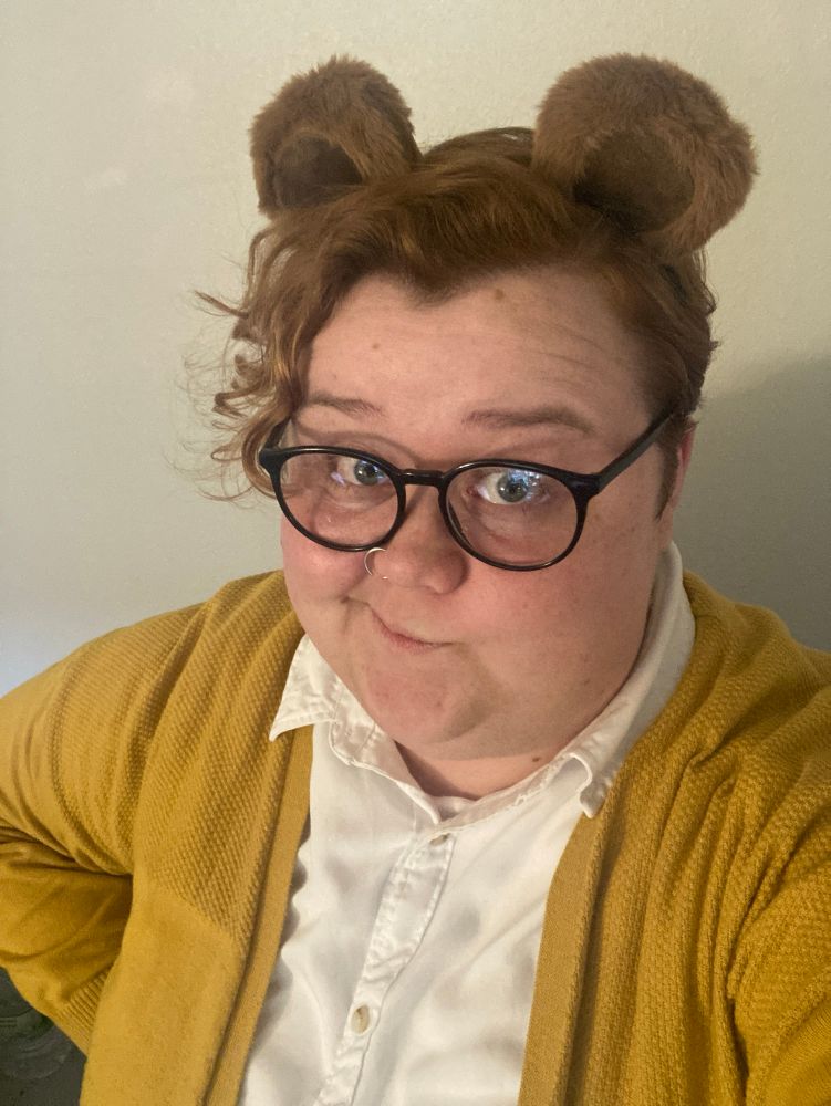 Sam in a yellow cardigan, white button up, black rimmed glasses, and brown bear ears for an Arthur costume.