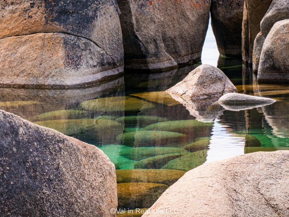 Close up of blue-green pool with smooth, submerged rocks surrounded by larger rocks rounded by erosion sticking out of the water in Lake Tahoe.