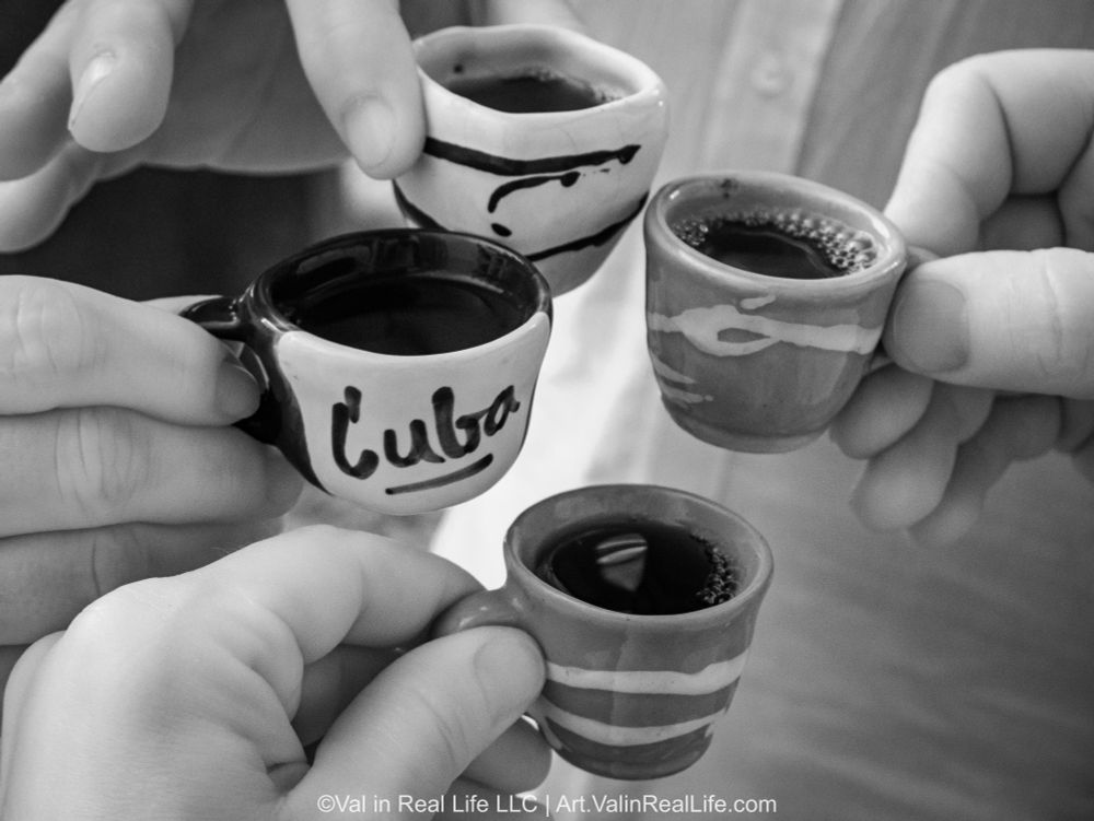 Close up of four espresso cups, one of which reads "Cuba", being held my for different hands extending into the frame by Val Weston.