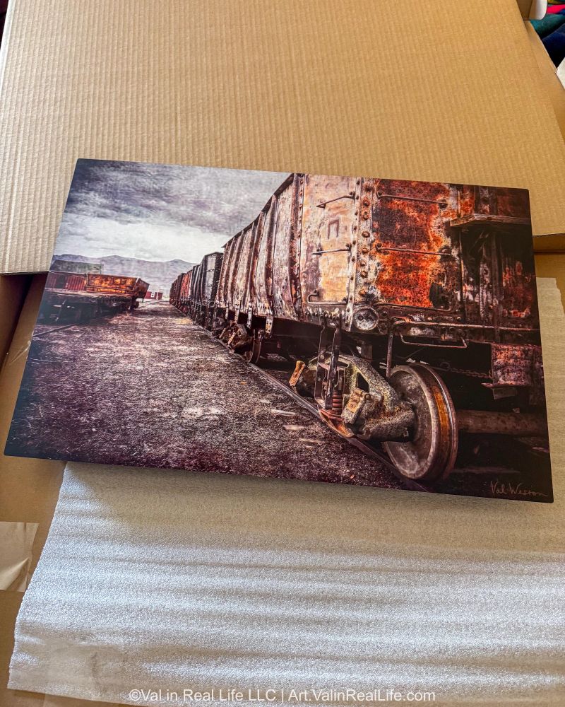 Metal photographic print of rusted train cars lying in open box.