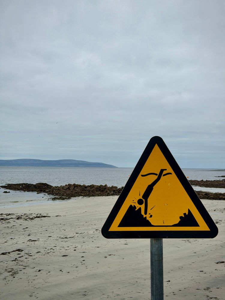 A safety warning sign on the beach at Galway Bay depicting a stick figure diving and hitting its head on a rock. 