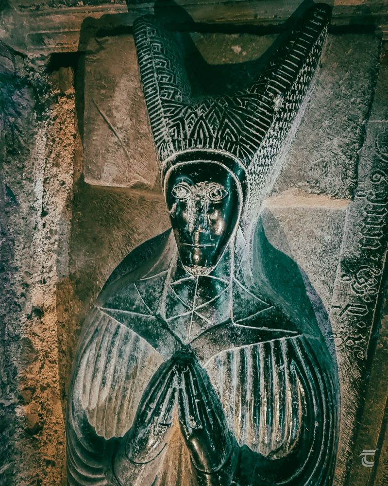 A stone medieval effigy of a woman in a tall headdress