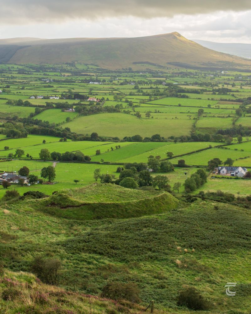 an early medieval ringfort, looking over green countryside towards distant mountains 