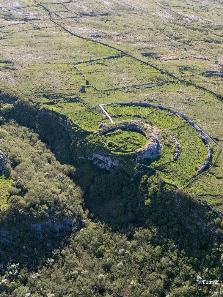 An aerial view of Cahercommaun a large early medieval circular stone fort in the Burren of County Clare Ireland. The drystone walls of the fort are adjacent to a steep ravine that has a forested bottom.