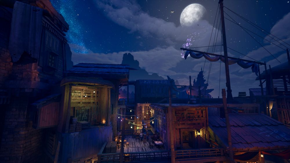 The moon hangs over a shantytown where a few people are gathered outside on a deck under strings of colorful lanterns.