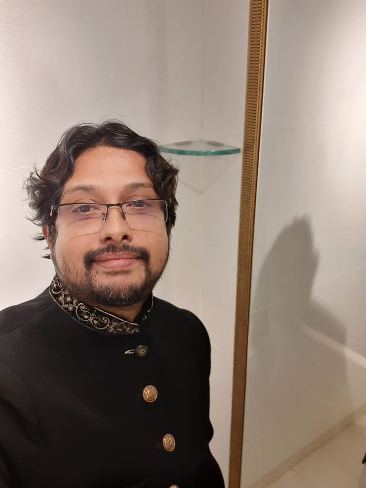 A selfie of me wearing a black sherwani suit. It has gold embroidery on the collar with gold colored buttons.