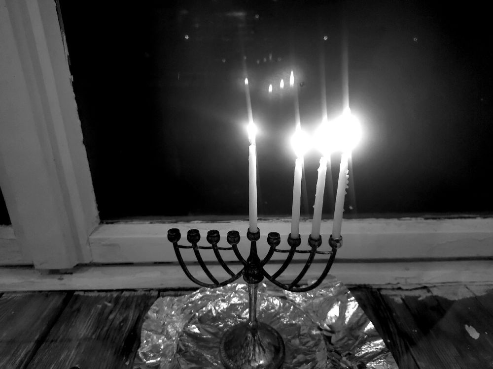 Schwarz-weiße Aufnahme eines Chanukka-Leuchters mit vier brennenden Kerzen auf einer Fensterbank.