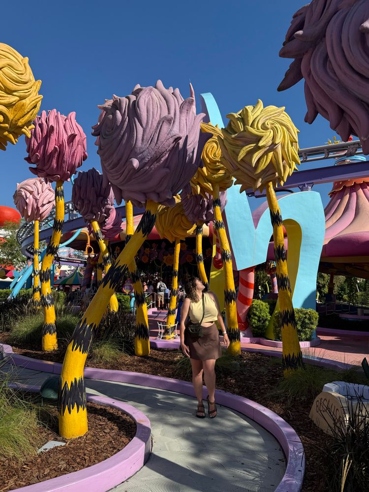 White female brown curly hair looking up at trees from the Lorax (yellow and black striped trunk and purple yellow and pink tops) 