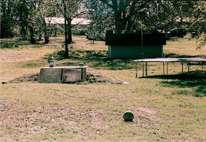 A tornado shelter, trampoline, and basketball on a lawn in rural Oklahoma.