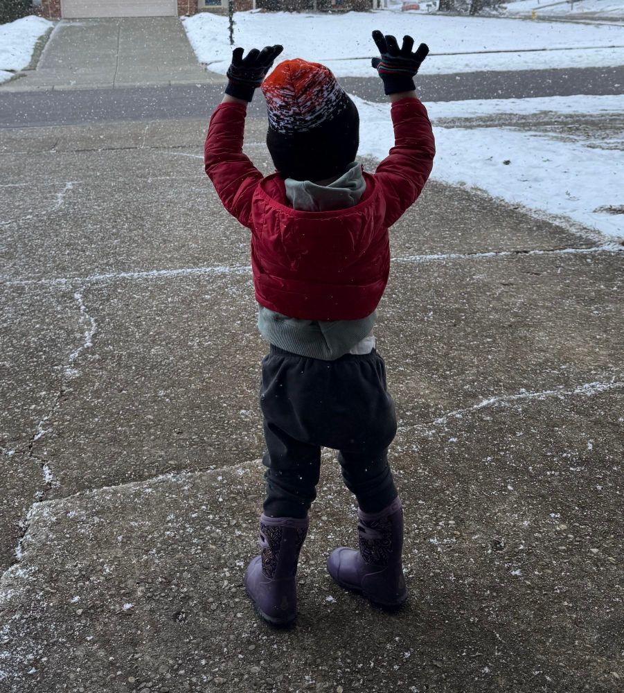 Little kid bundled up in a red coat raising their hands in the air as the snow falls