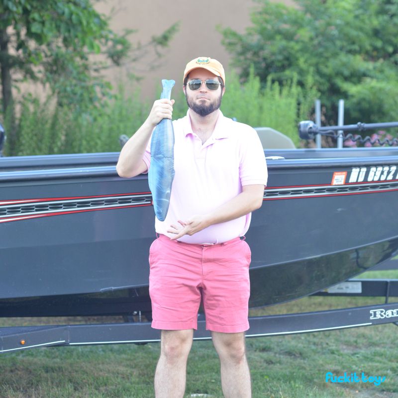 Kenton, in a pink polo shirt, crappy aviator sunglasses, an orange ball cap with a logo on it, and magenta boat shorts. He's holding an enormous silicone fish by the tail that goes from his navel to his eyebrows, and is showing it off like he caught it, the prick.