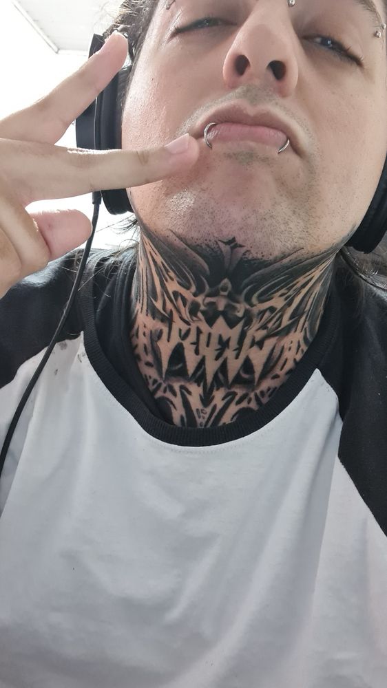 picture of a very beautiful white guy giving a sideways peace sign, wearing a white shirt and headphones. his neck has a sick abstract tattoo that makes him look very cool