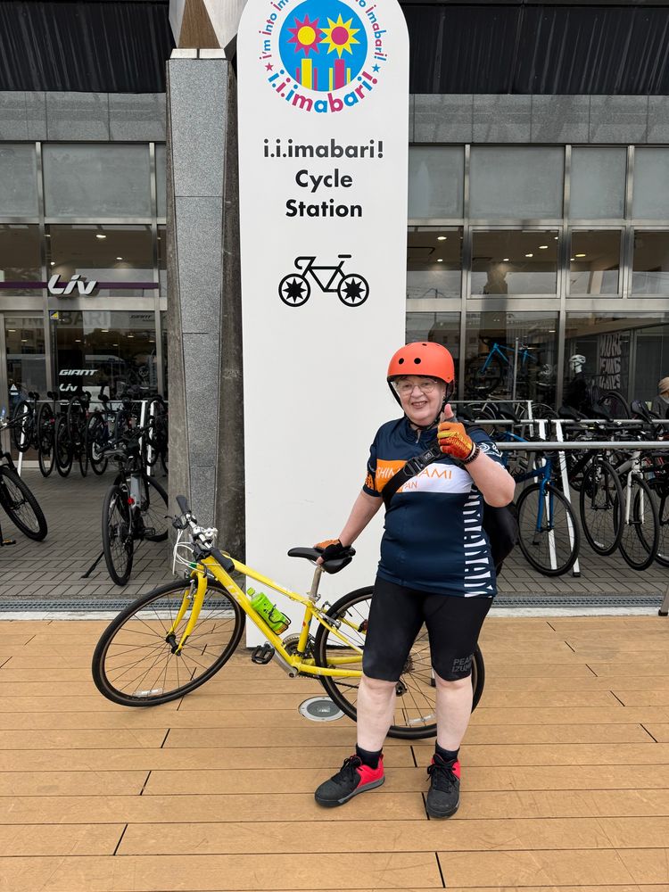 Me with an orange helmet and a yellow bicycle giving a thumbs up by the bicycle return post at the end of the Shimanami Kaido 