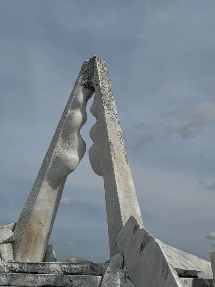 Top of a hill on a beautiful day. A white stone statue resembling a two hands brought together