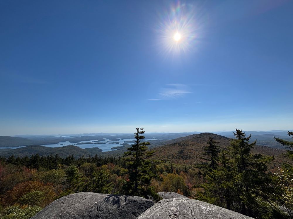 View from mountain summit - few small trees and boulders in foreground, Autumn colors, lakes, blue sky
