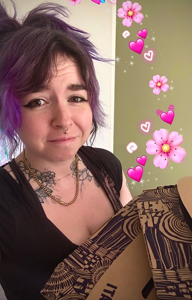 Connie holding pizza boxes with pink emojis around them. Connie has a thankful? expression