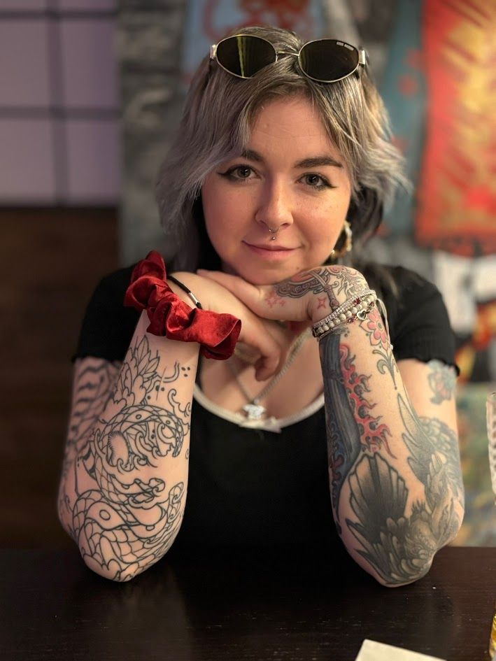 connie smiling for the camera with their elbows on the table and their hands resting under their chin