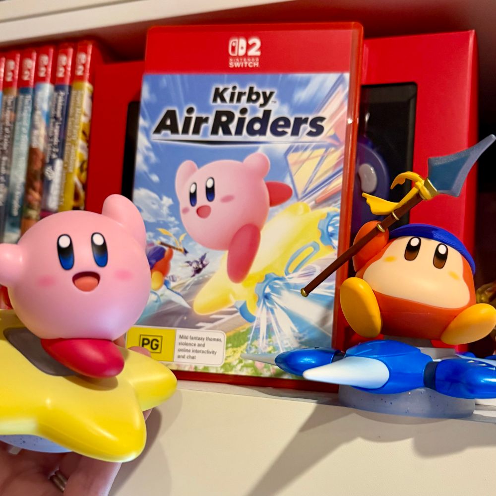 Photo of Kirby Air Riders for Nintendo Switch 2 (NS2) alongside the Kirby & Warp Star amiibo and Bandana Waddle Dee & Winged Star amiibo. Our NS2 collection is in the background.
