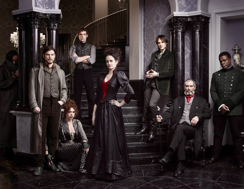 The cast of the TV show Penny Dreadful, posing at the foot of the spiral staircase of a grand black- and gray-decorated marbled foyer.